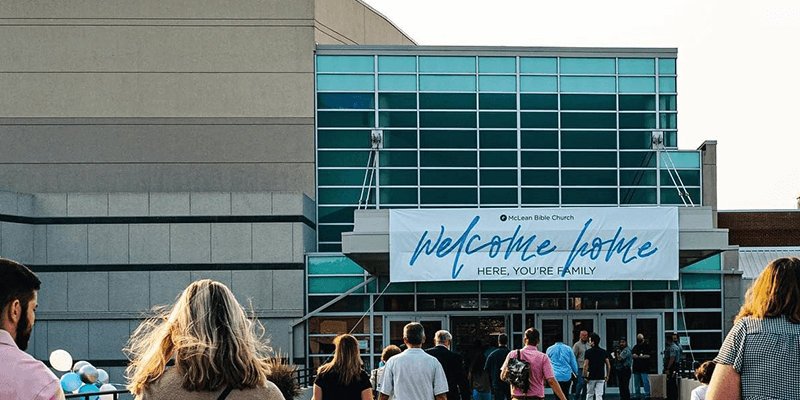 Congregants gathering at McLean Bible Church entrance with a ‘Welcome Home’ sign