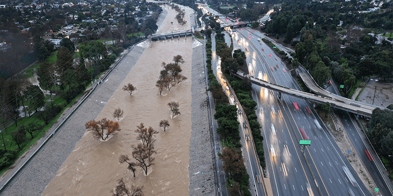 LA River swollen by storm runoff with nearby highway during atmospheric river storm”
